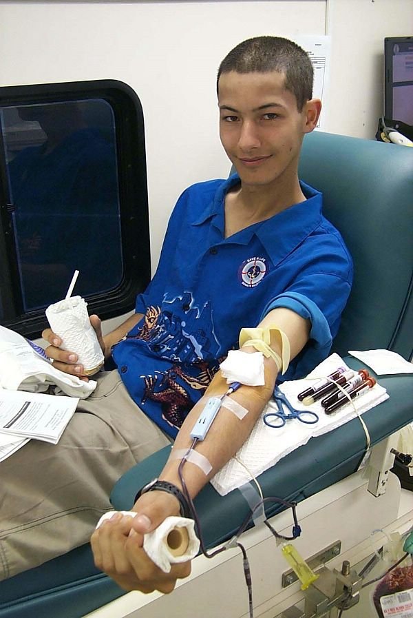 Person donating blood while seated at a blood collection station